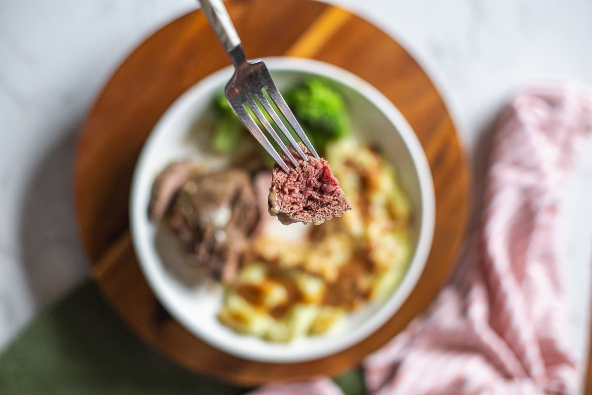 bite of medium rare air fryer sirloin steak on fork above plate of food.