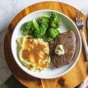 air fryer sirloin steak topped with herb butter beside broccoli, mashed potatoes, and utensils.