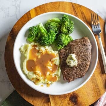 air fryer sirloin steak topped with herb butter beside broccoli, mashed potatoes, and utensils.