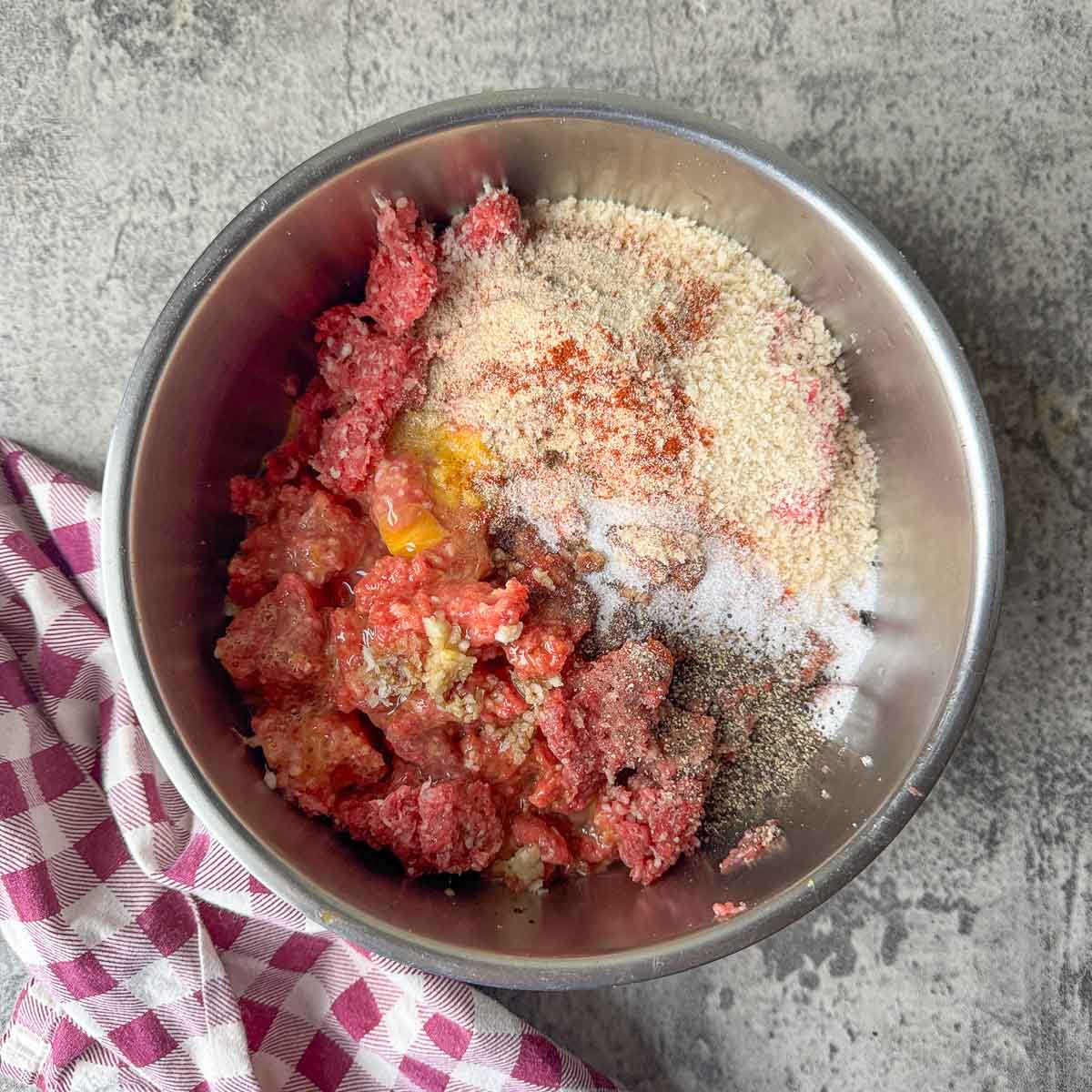 a bowl with Salisbury steak ingredients with a checkered napkin next to it