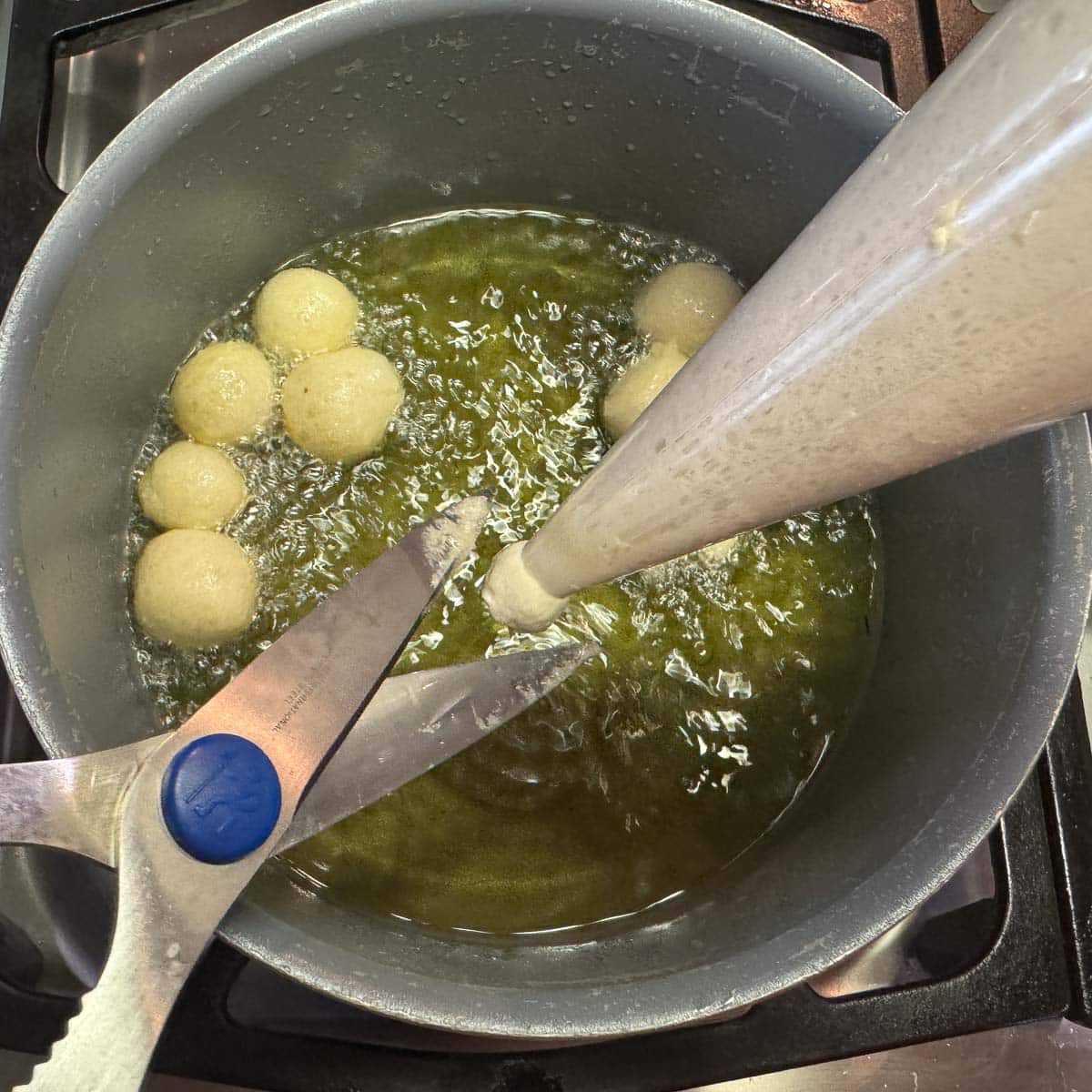 slicing batter from piping bag into hot oil