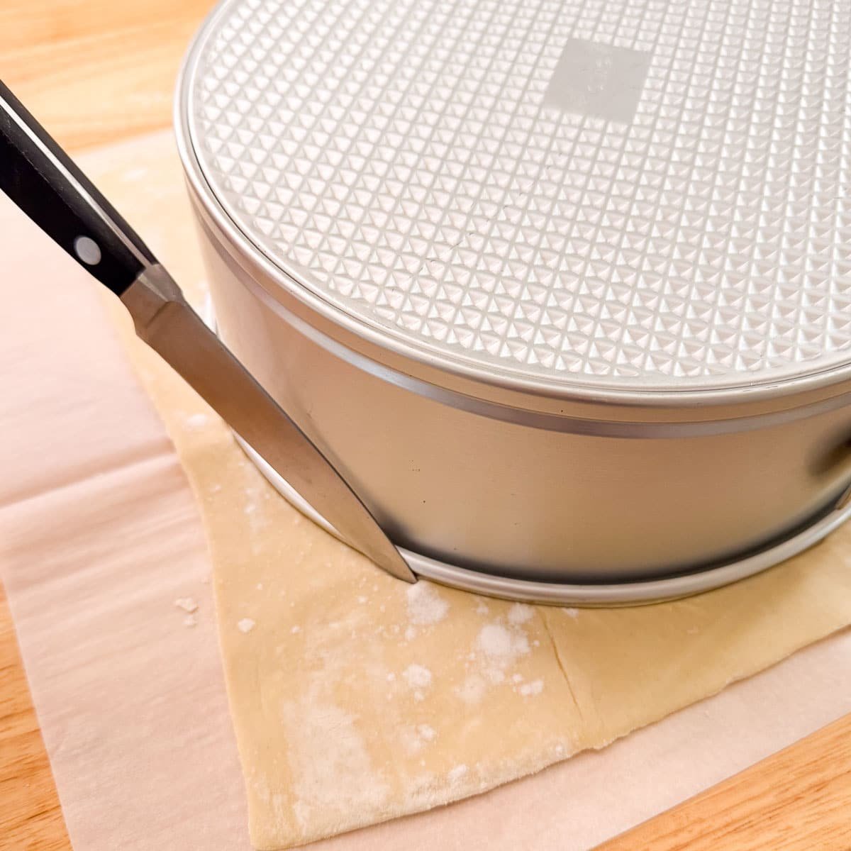 knife cutting puff pastry around the edge of a cake pan.