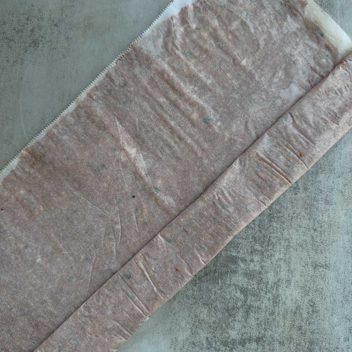 doner kebab meat mixture being rolled between two sheets of parchment paper