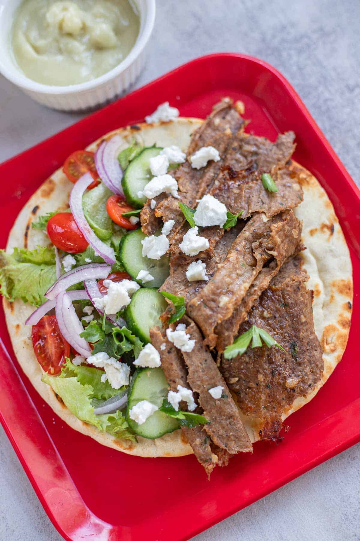 homemade doner kebab topped with fresh veggies and feta on a red plate
