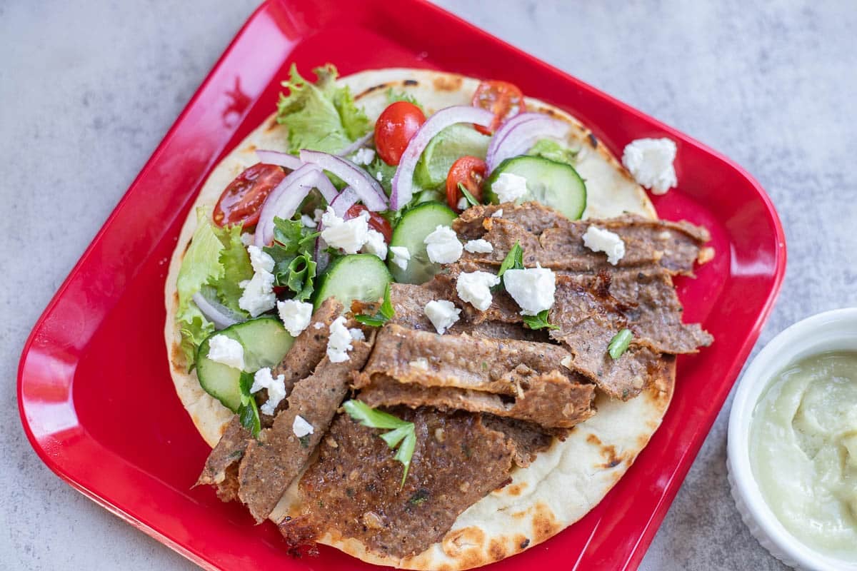 red plate with pita bread, veggies, and doner kebab