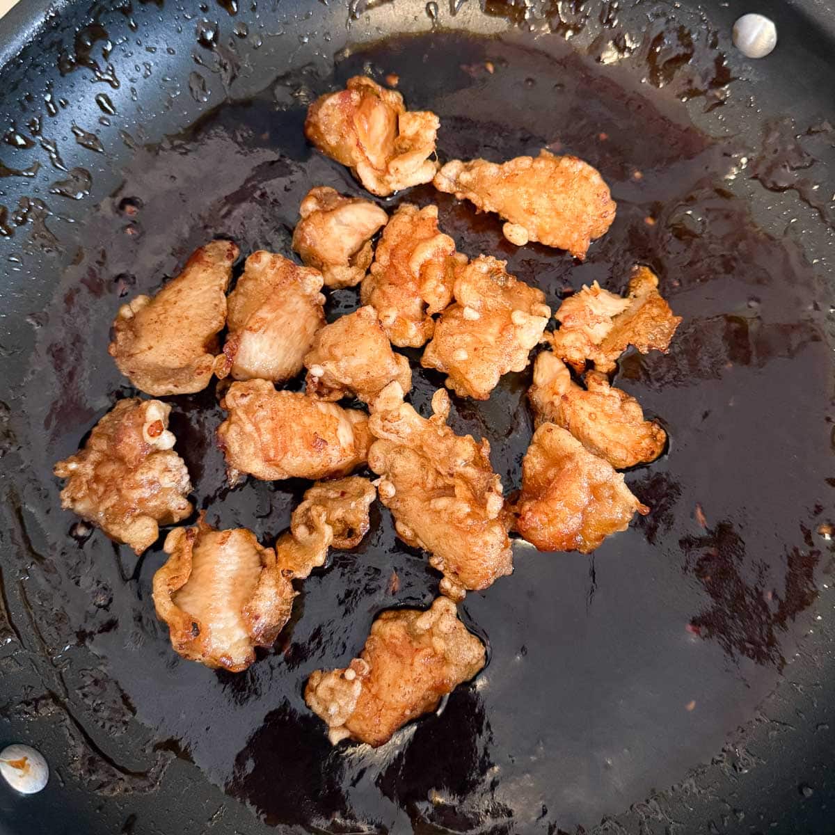 pieces of chicken in pan with sticky sesame sauce.