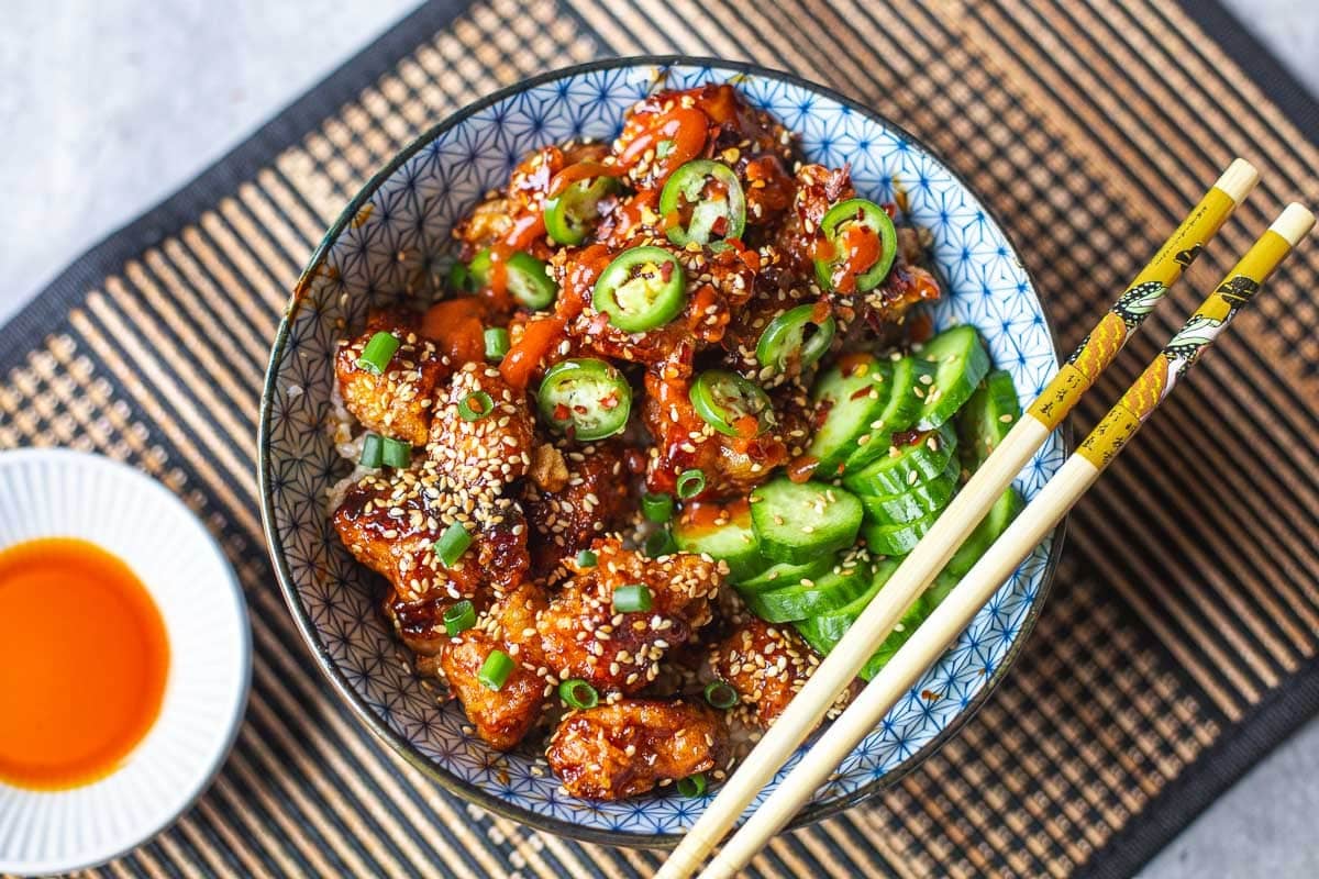 sticky sesame chicken with cucumbers and side of chili oil and chopsticks.