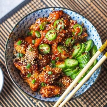 sticky sesame chicken with cucumbers and side of chili oil and chopsticks.