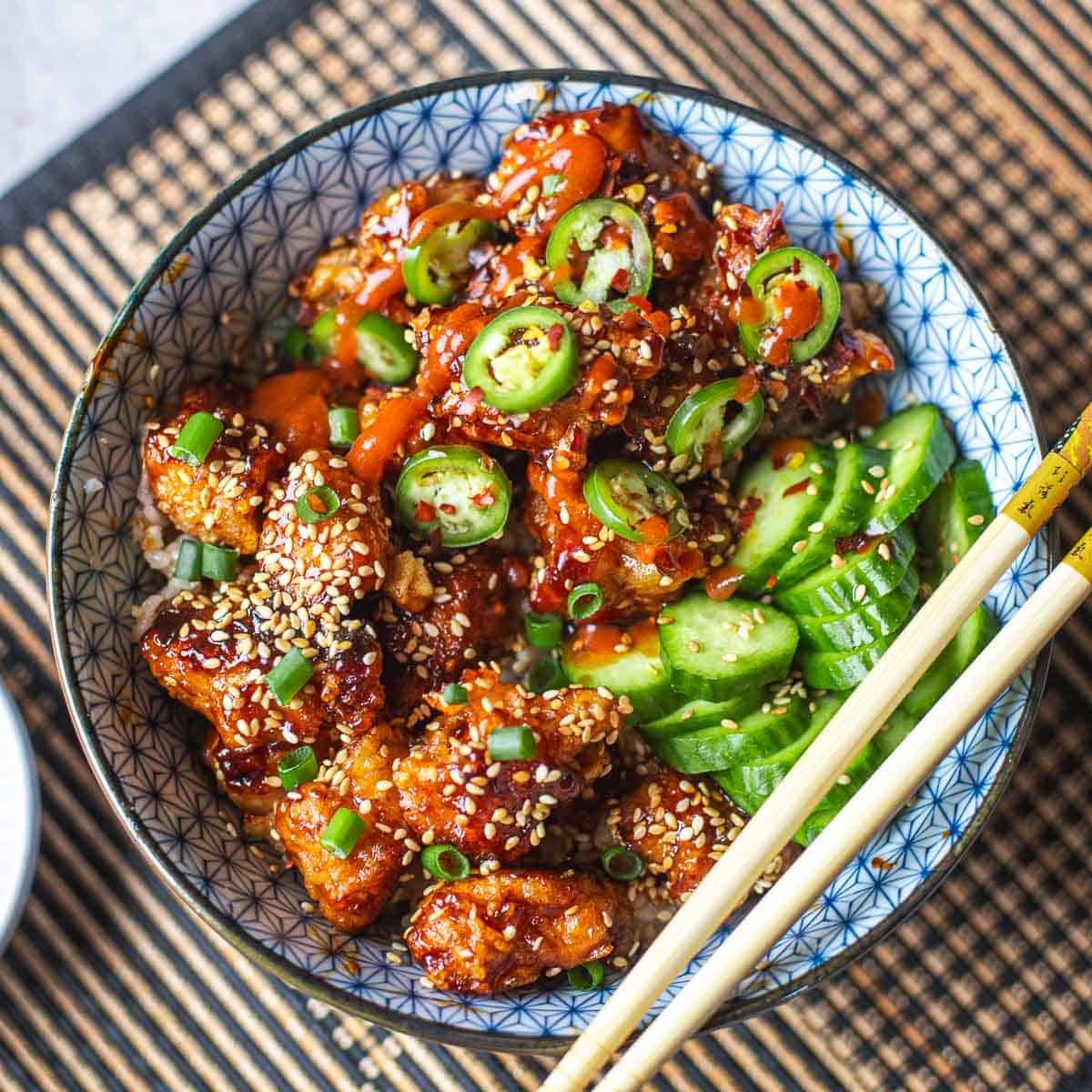 sticky sesame chicken with cucumbers and side of chili oil and chopsticks.