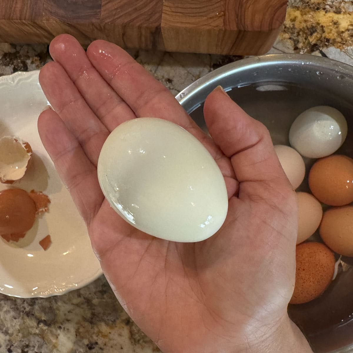 peeled eggs in an open hand with eggs and peels below it