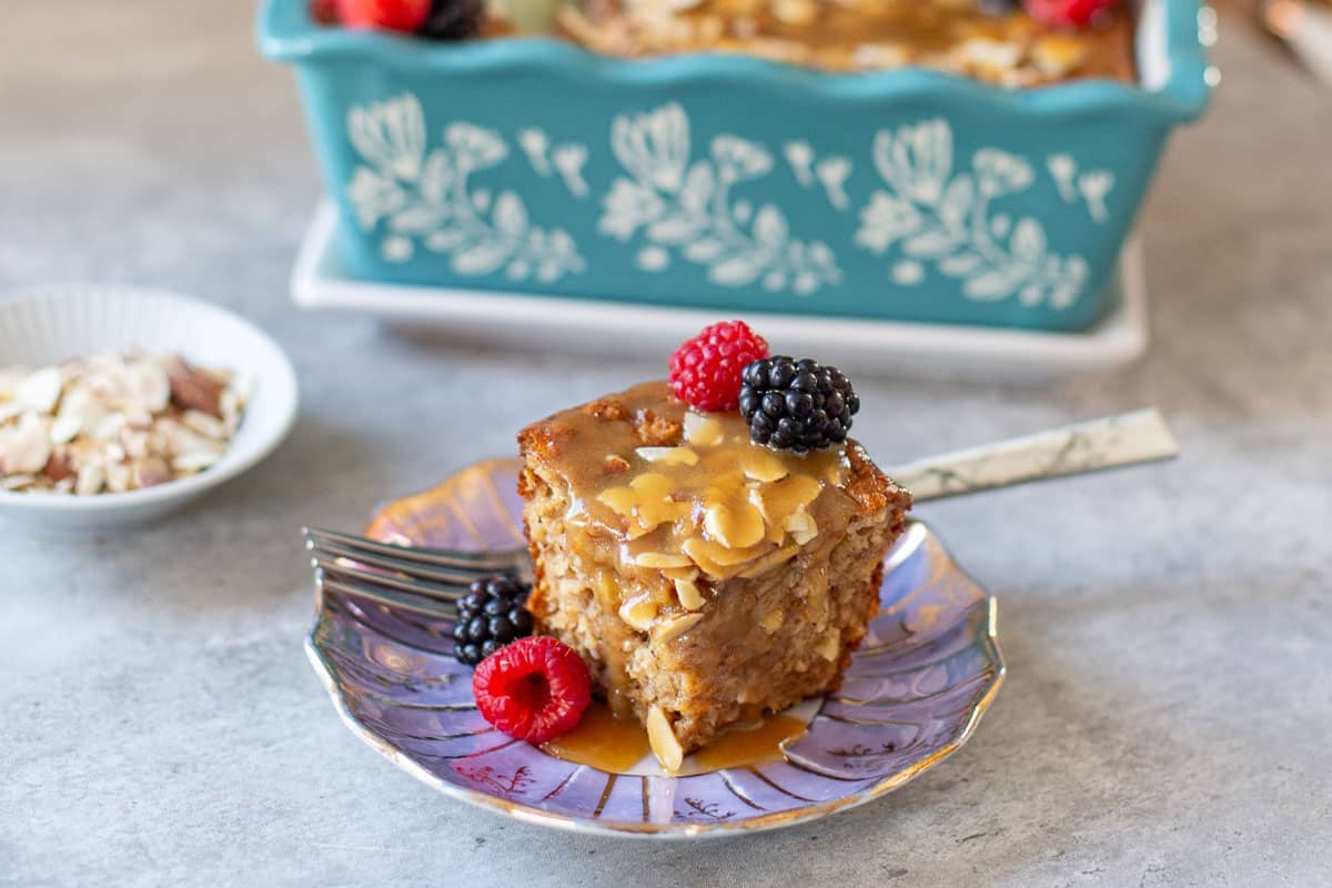 slice of baked protein oats with fresh respberries and blackberries beside loaf pan and plate of slivered almonds.