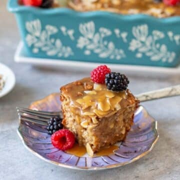 slice of baked protein oats with fresh respberries and blackberries beside loaf pan and plate of slivered almonds.