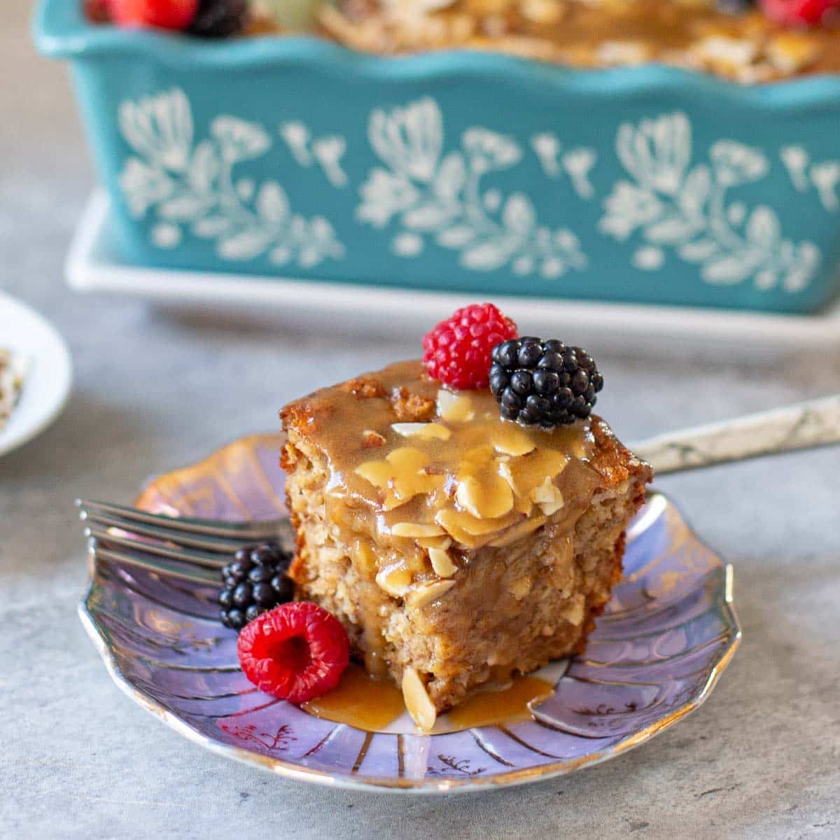 slice of baked protein oats with fresh respberries and blackberries beside loaf pan and plate of slivered almonds.