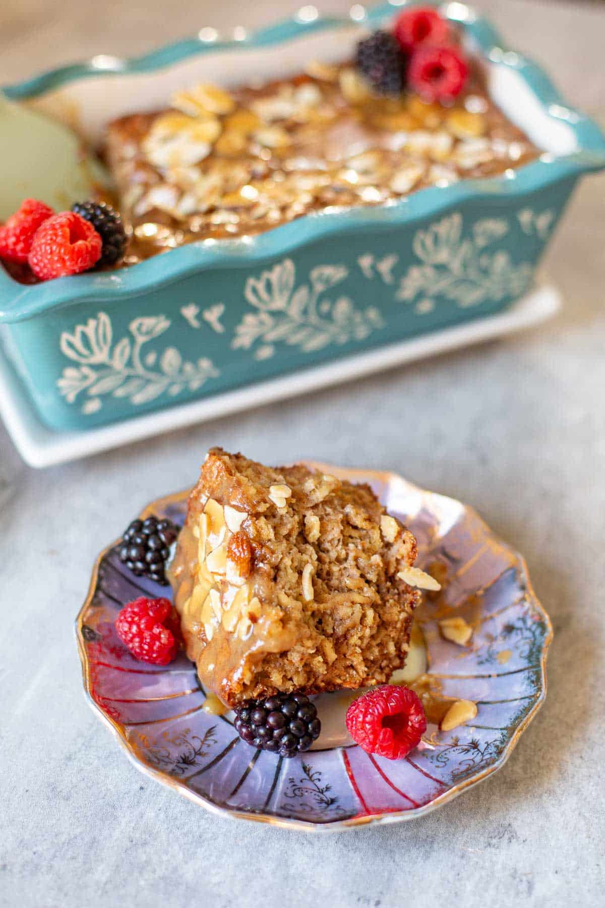 slice of baked protein oats with fresh respberries and blackberries beside loaf pan and plate of slivered almonds.