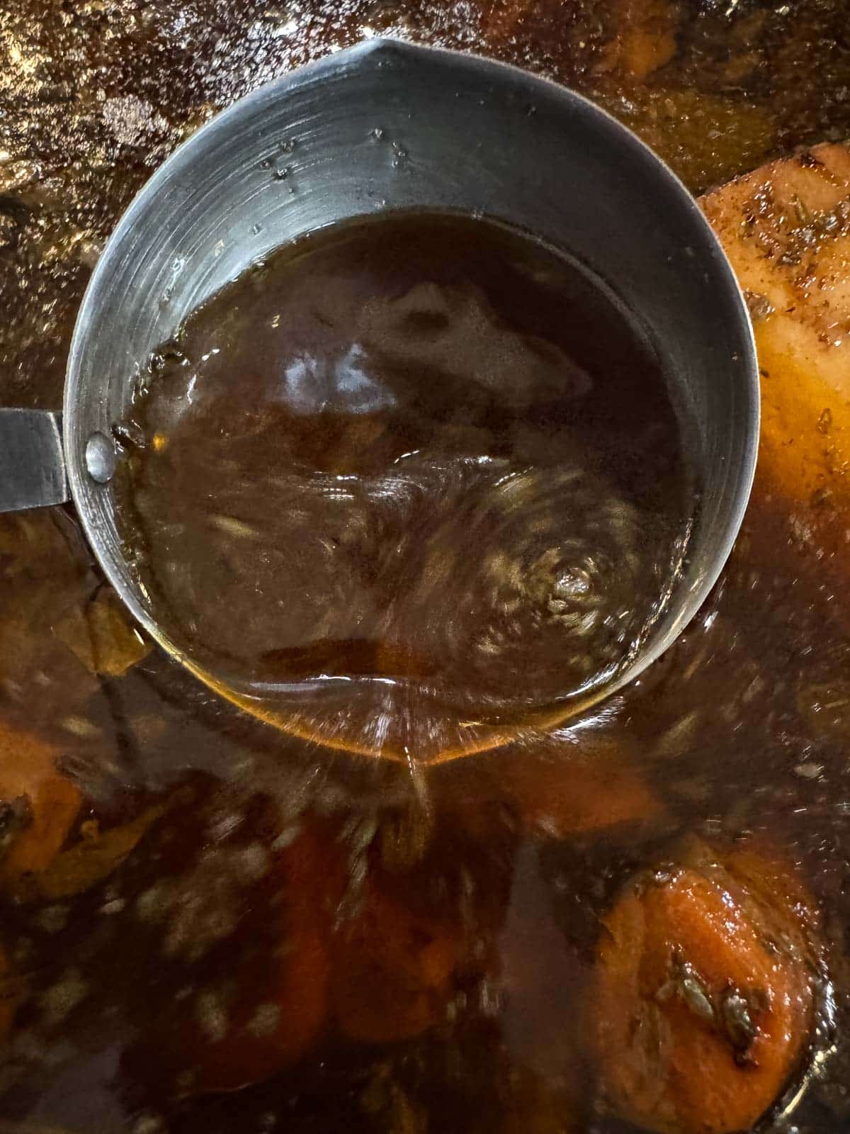 a ladle full of beef bone broth with more bone broth beneath it