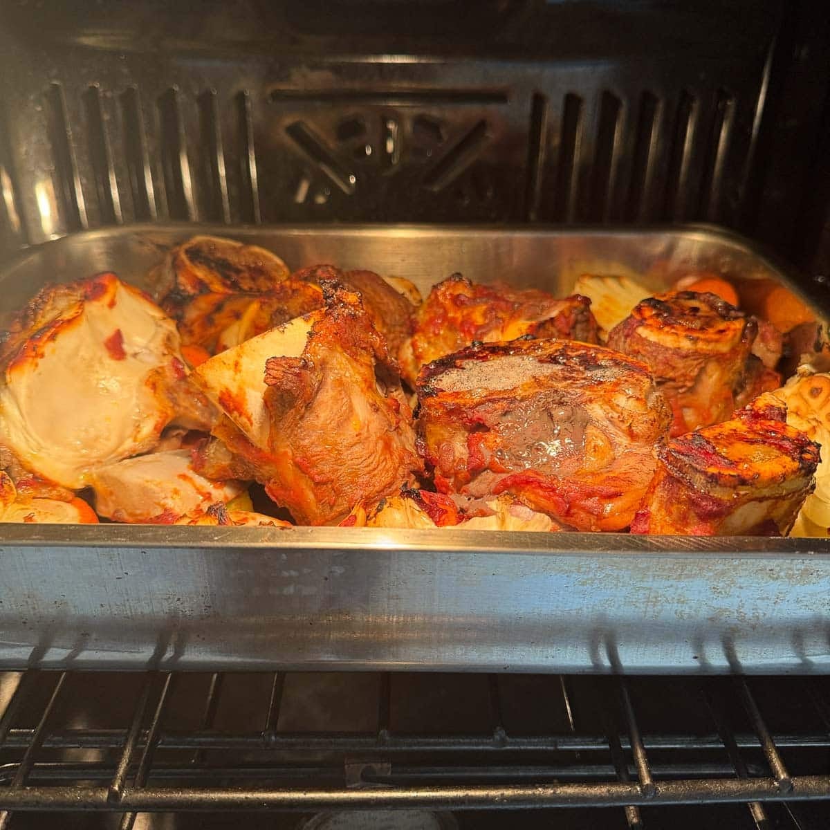 a pan of soup bones and veggies in a roasting pan in the oven