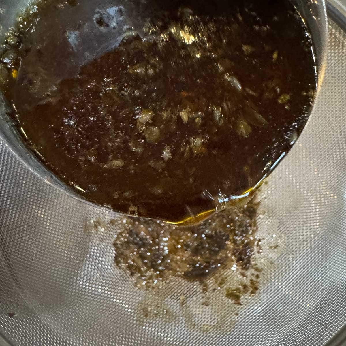straining beef bone broth through a fine mesh strainer