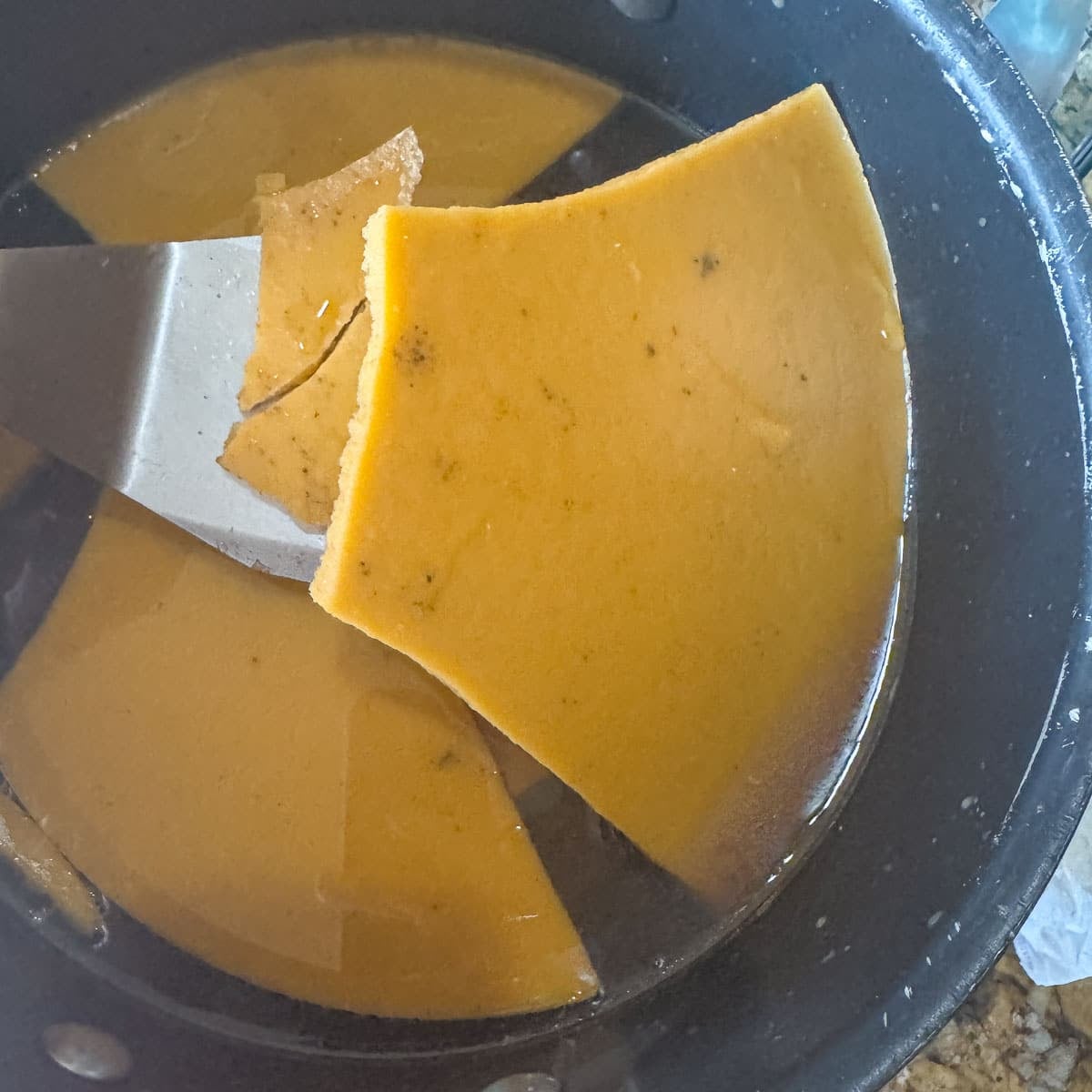 removing a layer of hardened fat from beef bone broth in a pot
