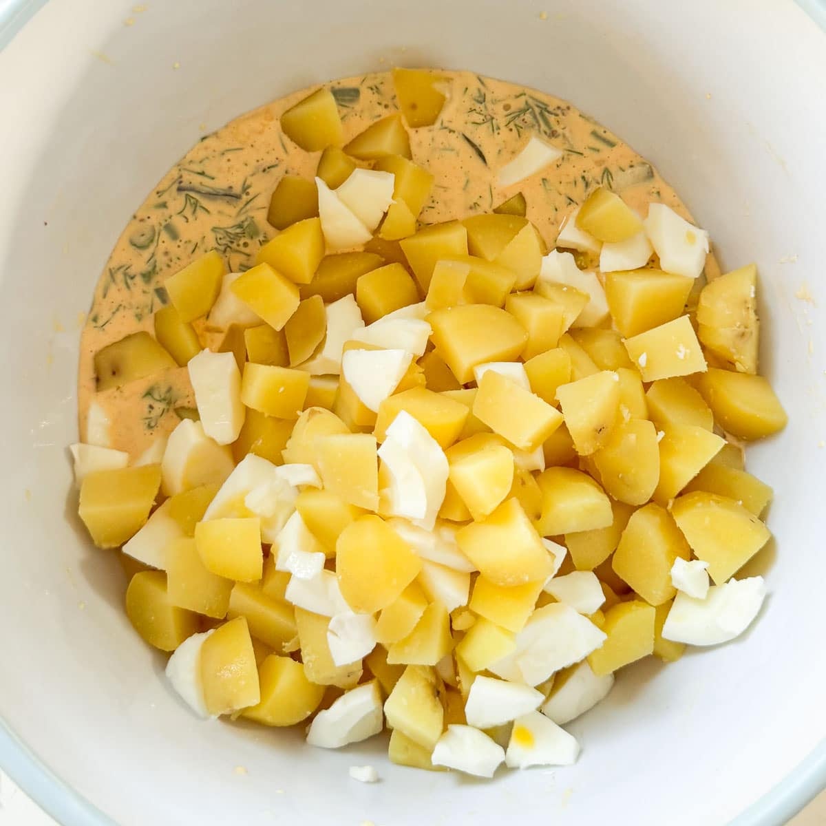 diced potatoes, eggs, and dressing in a white bowl