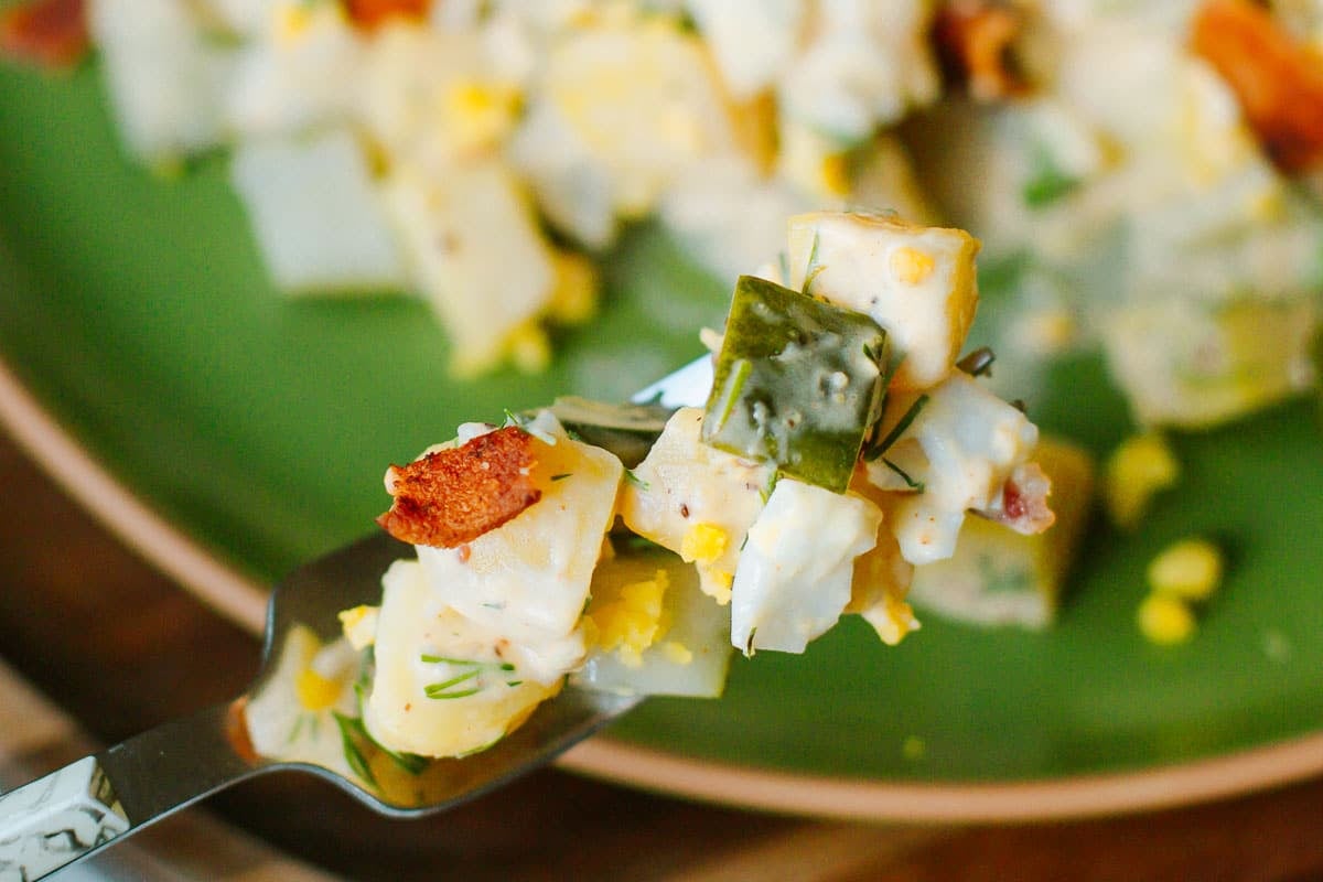 close up of dill pickle potato salad on a fork over a plate
