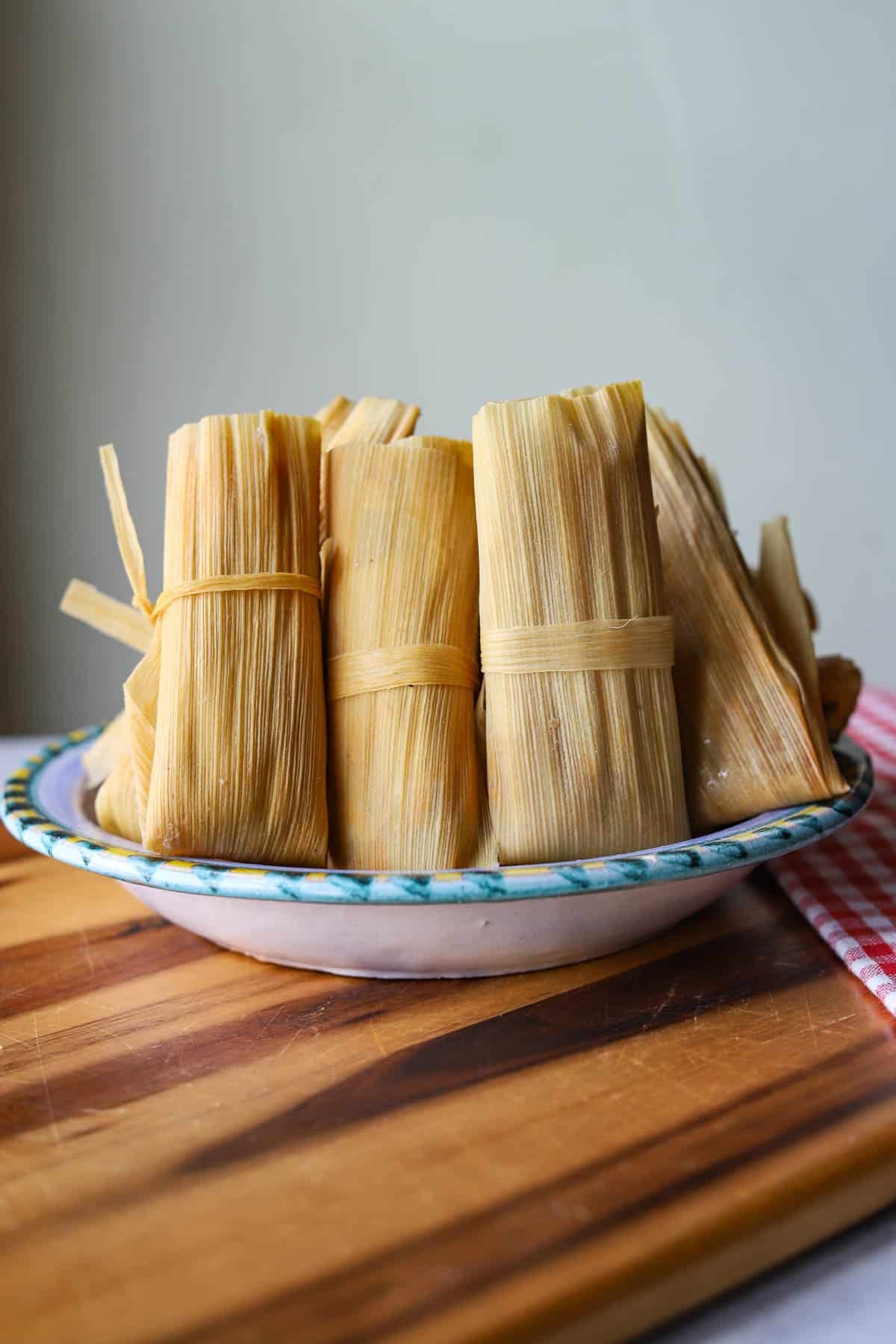 bowl with tamales on a wooden cutting board with red and white checkered napkin next to it