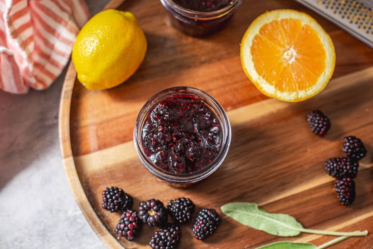 jar of blackberry jam beside fresh fruit and sage.