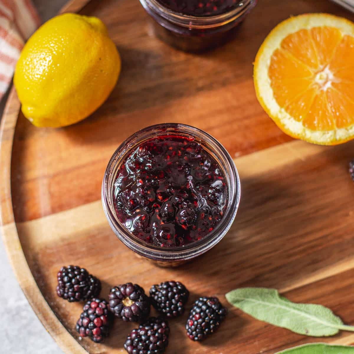 jar of blackberry jam beside fresh fruit and sage.