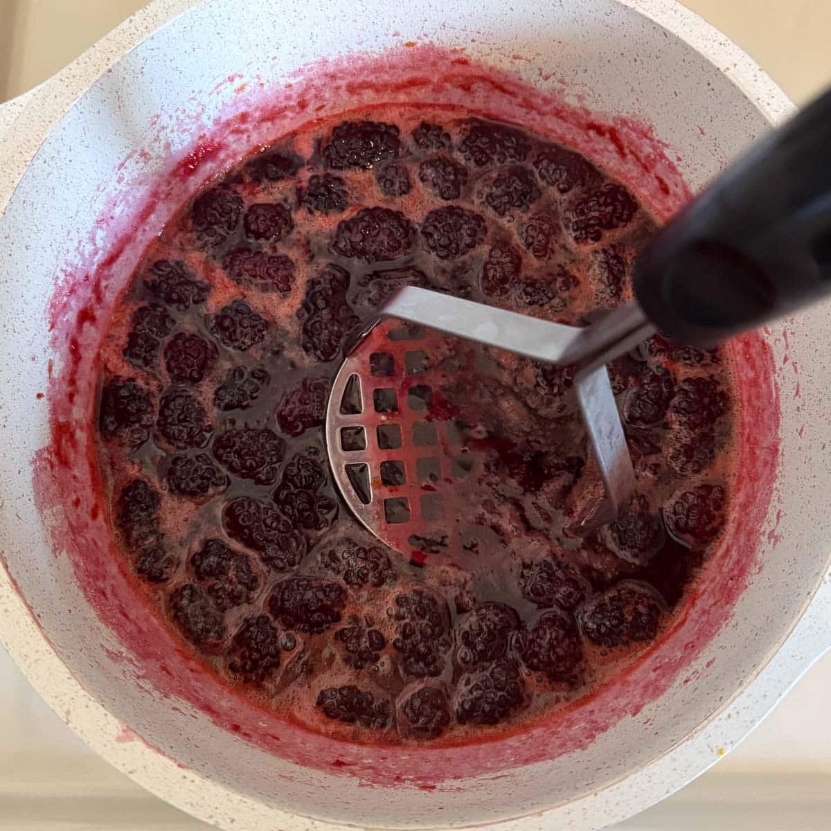 potato masher smashing blackberries in jam.