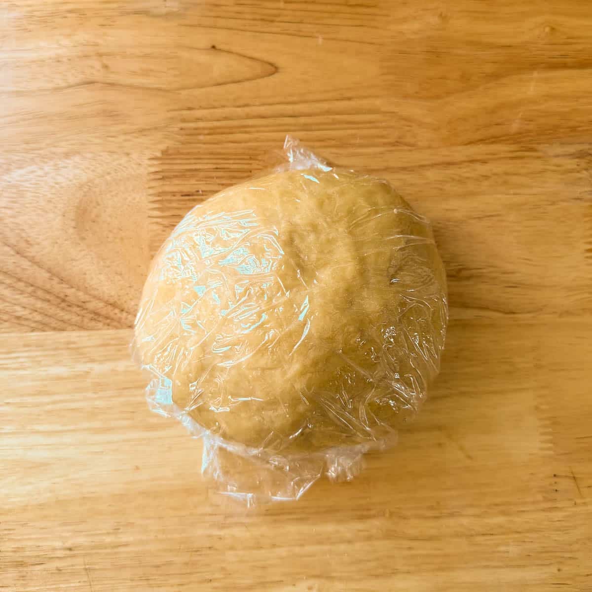 homemade egg noodle recipe dough ball covered in plastic wrap.