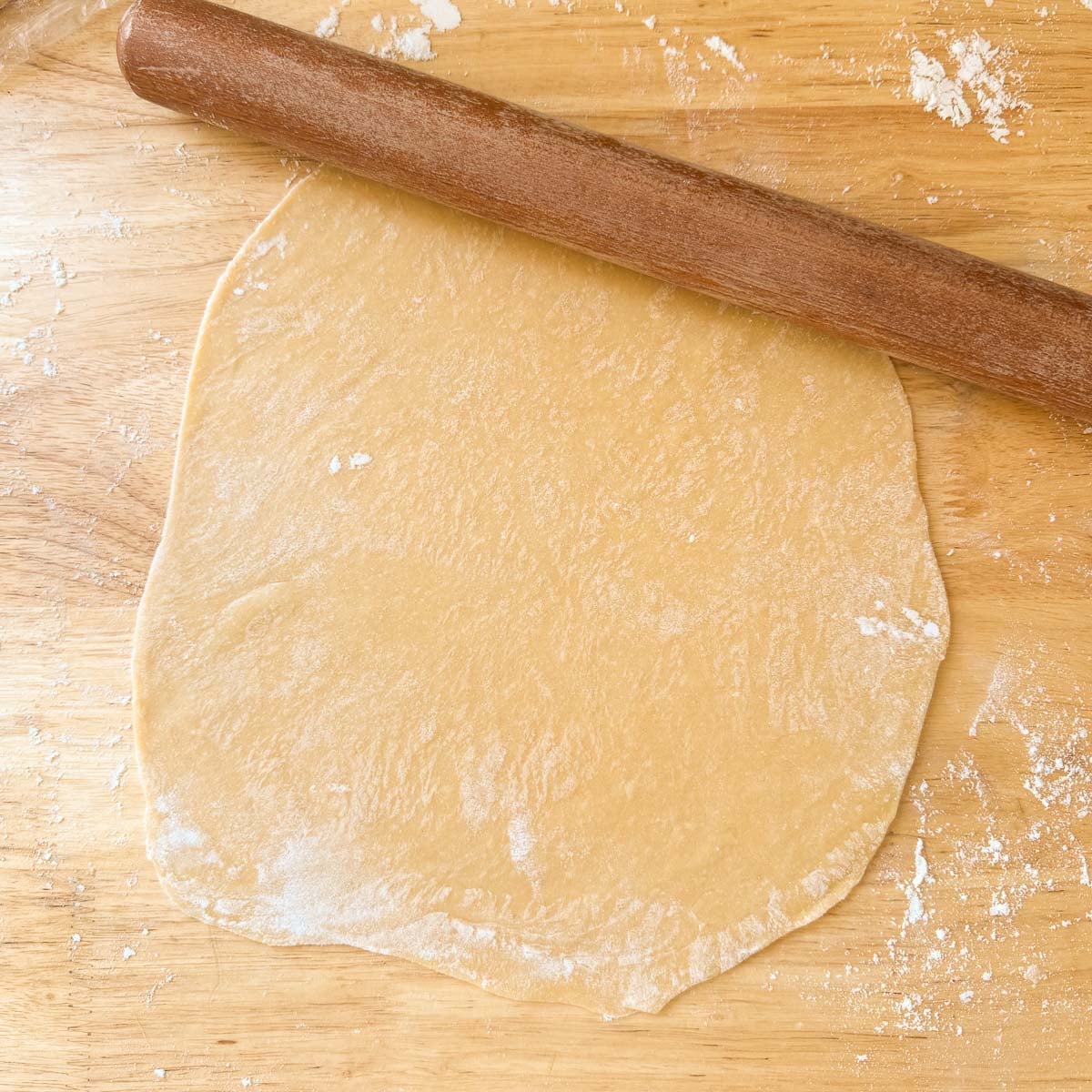 egg noodle dough being rolled with rolling pin.