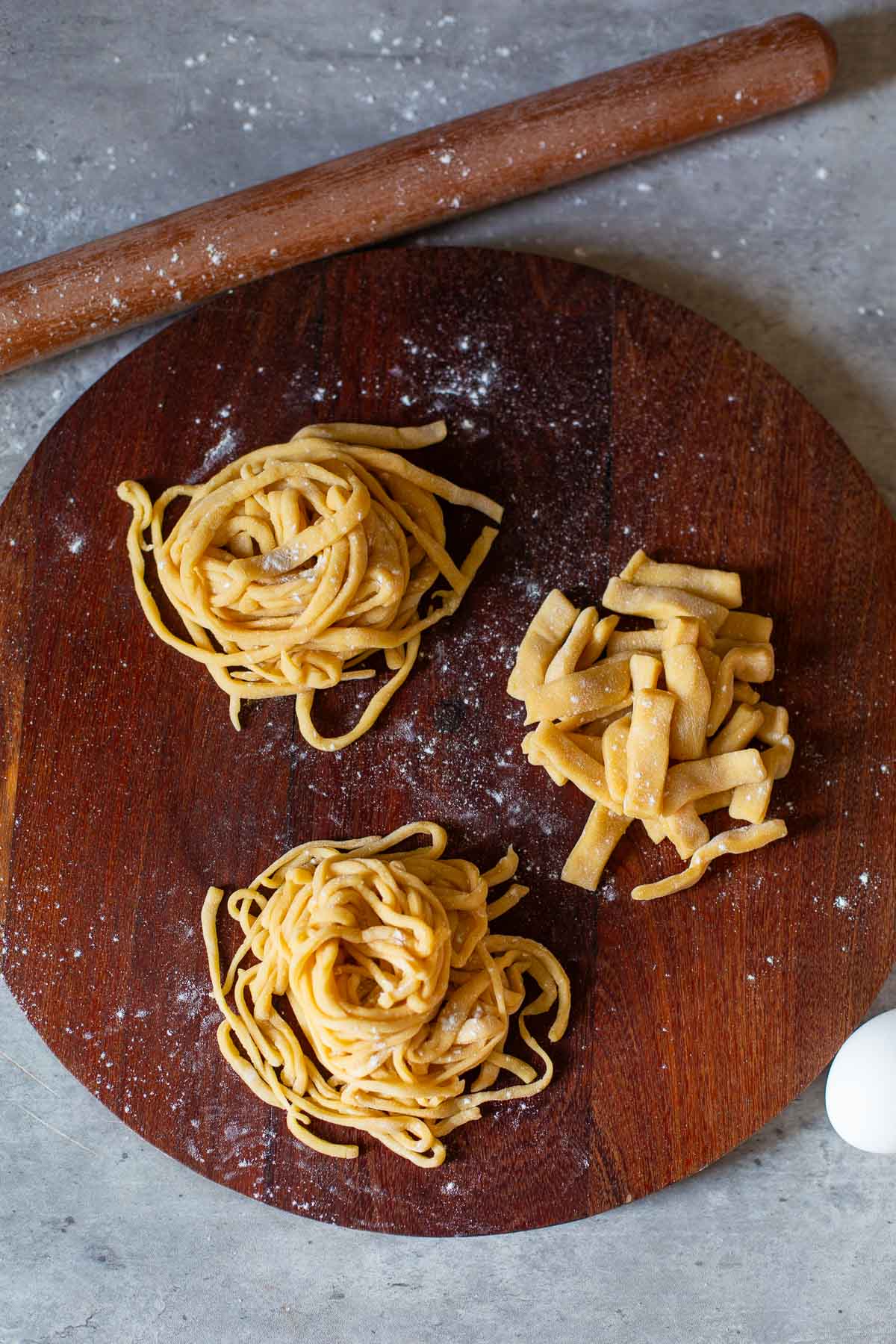 homemade egg noodles cut into three shapes: short & thick noodles, medium width noodles, and thin, delicate noodles beside rolling pin and eggs.
