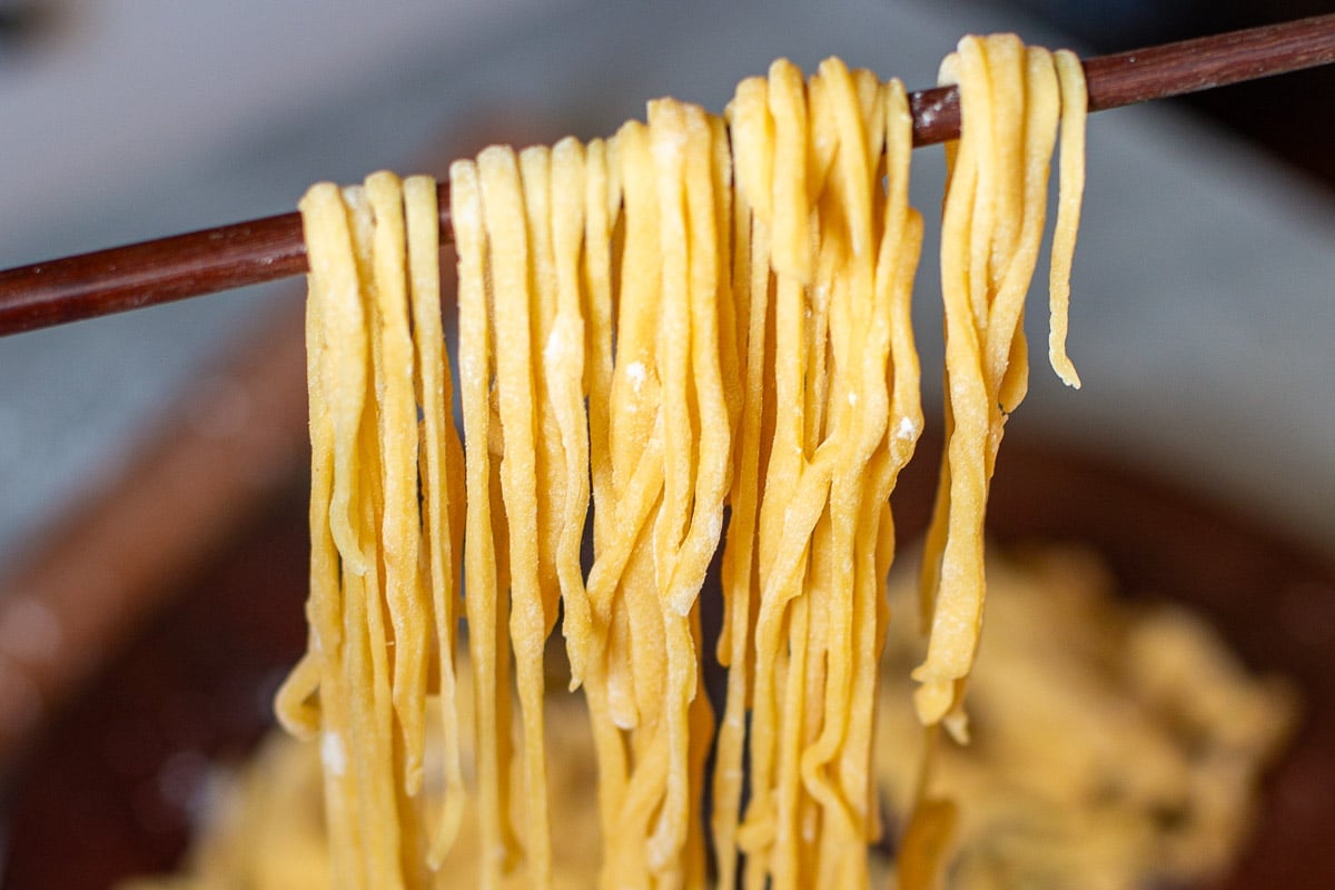 thinly sliced egg noodles dangling over chopstick.