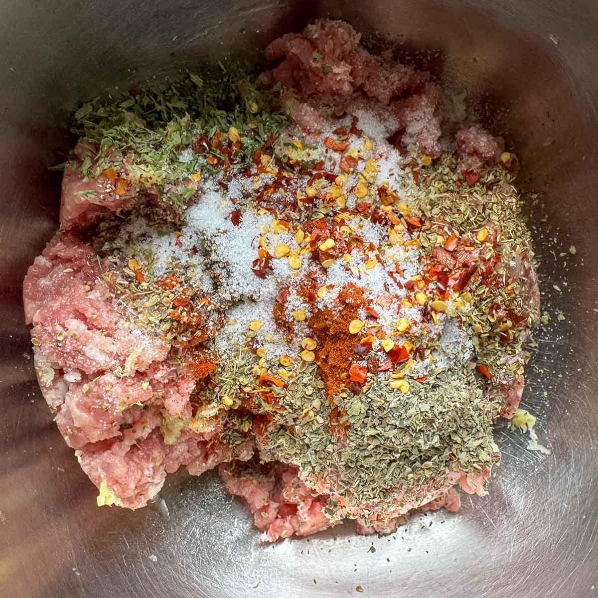 ground pork in a bowl, topped with spices and herbs