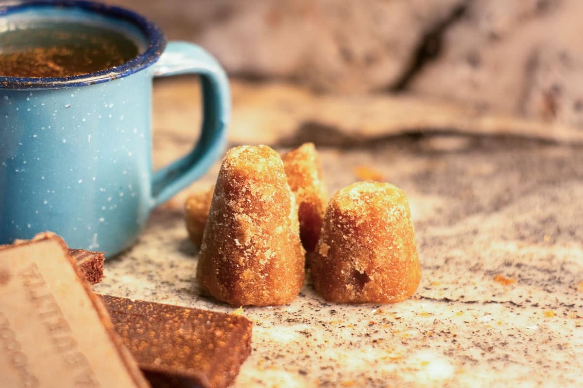 piloncillo cone beside blue mug and pieces of chocolate.