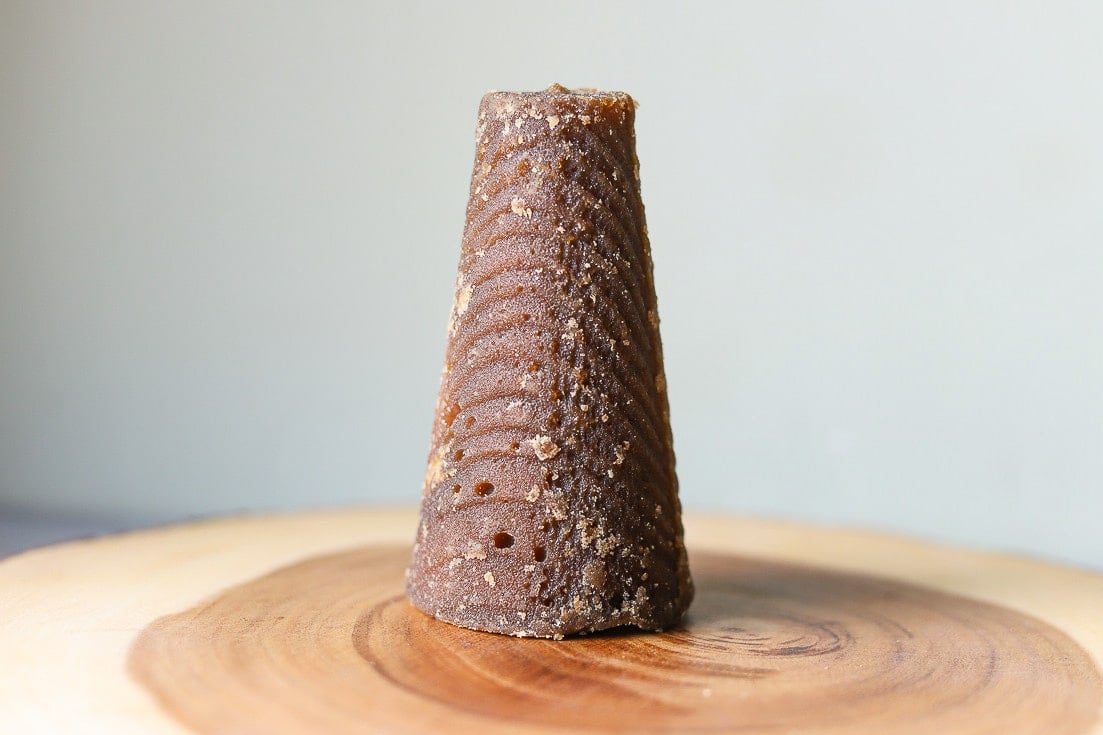 cone-shaped panela (piloncillo, rapadura) on a wooden cutting board.
