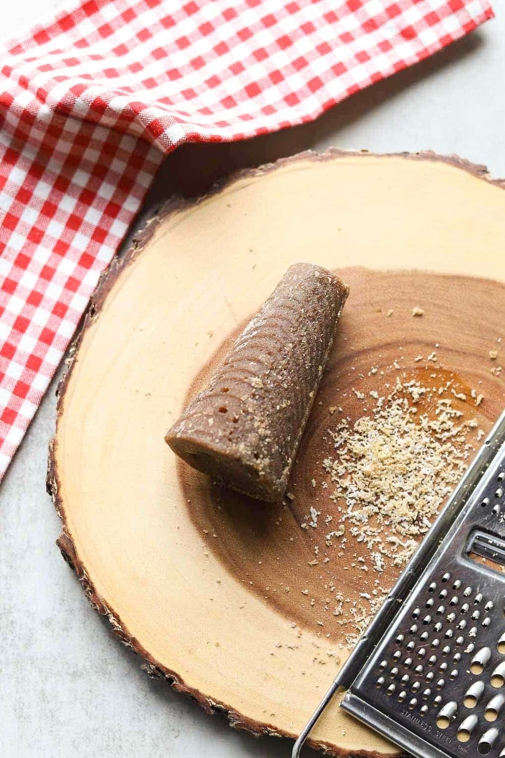 cone-shaped panela (piloncillo, rapadura) on a wooden cutting board with gingham towel and cheese grater and small pile of grated sugar.
