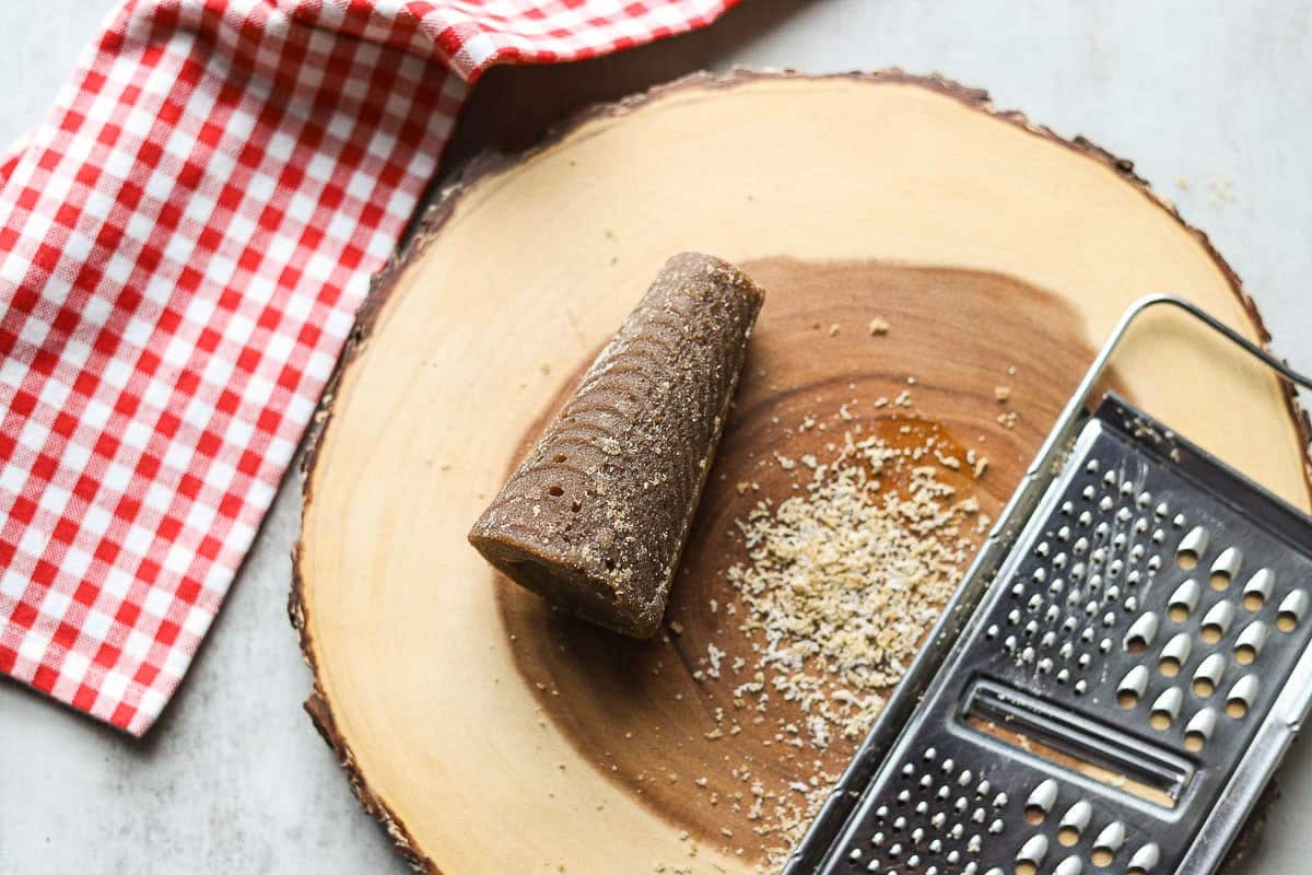 cone-shaped panela (piloncillo, rapadura) on a wooden cutting board with gingham towel and cheese grater and small pile of grated sugar.