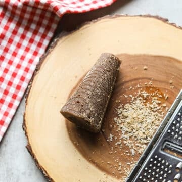 cone-shaped panela (piloncillo, rapadura) on a wooden cutting board with gingham towel and cheese grater and small pile of grated sugar.