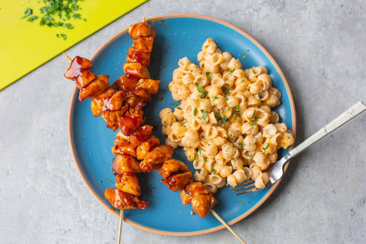 air fryer bbq chicken on skewers on a blue plate beside mac and cheese.