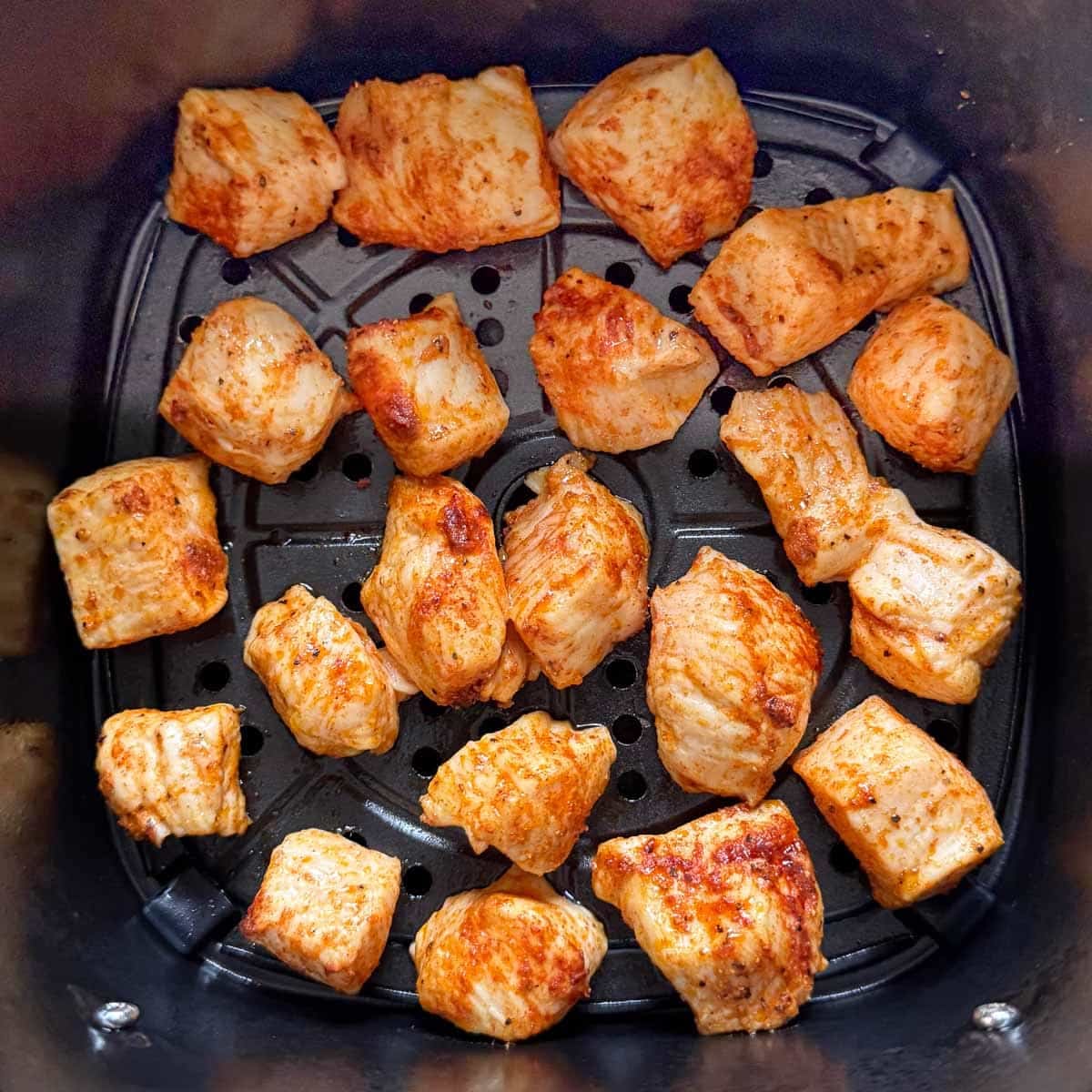 cubed BBQ chicken in air fryer basket after cooking one side.