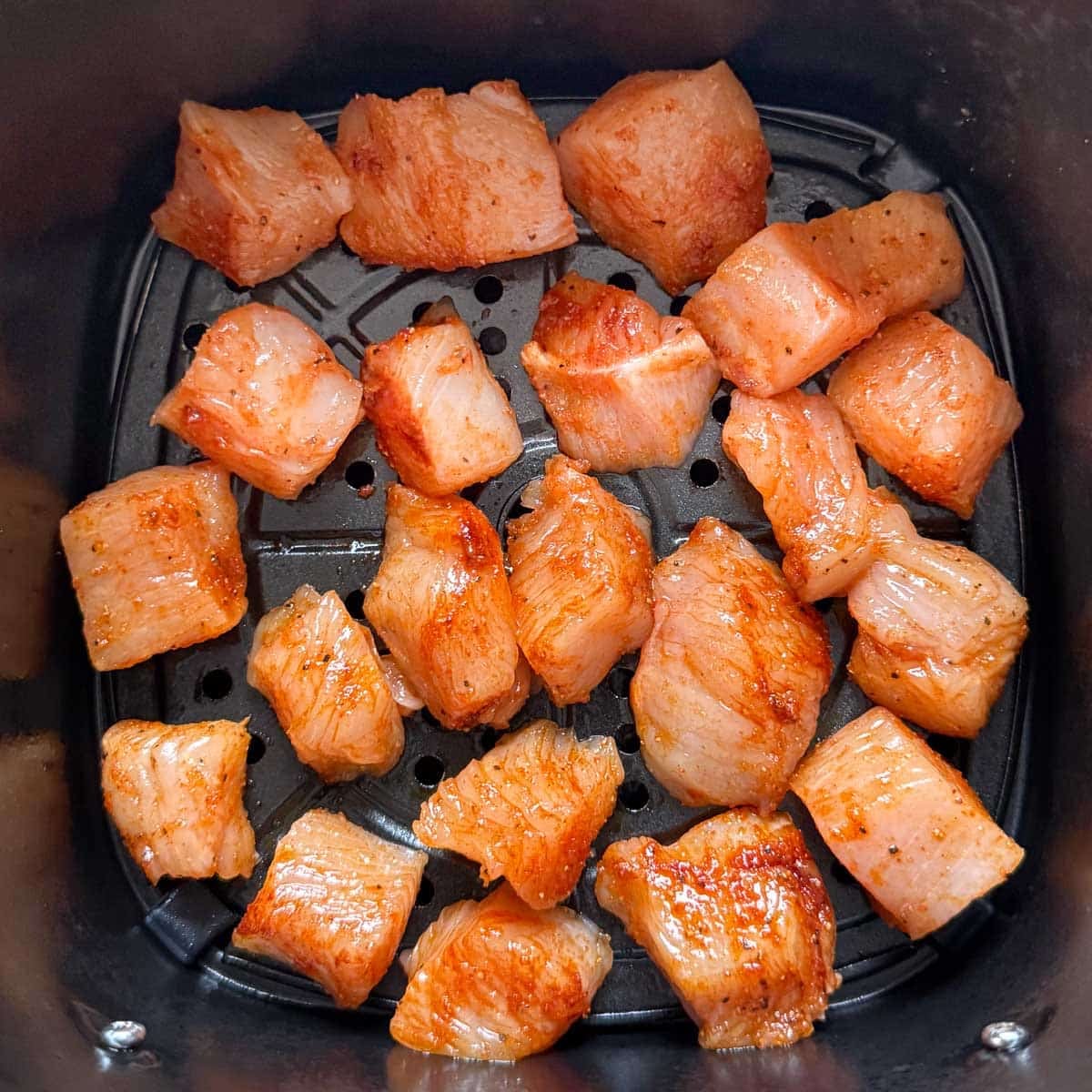 raw seasoned chicken in a single layer in air fryer basket.