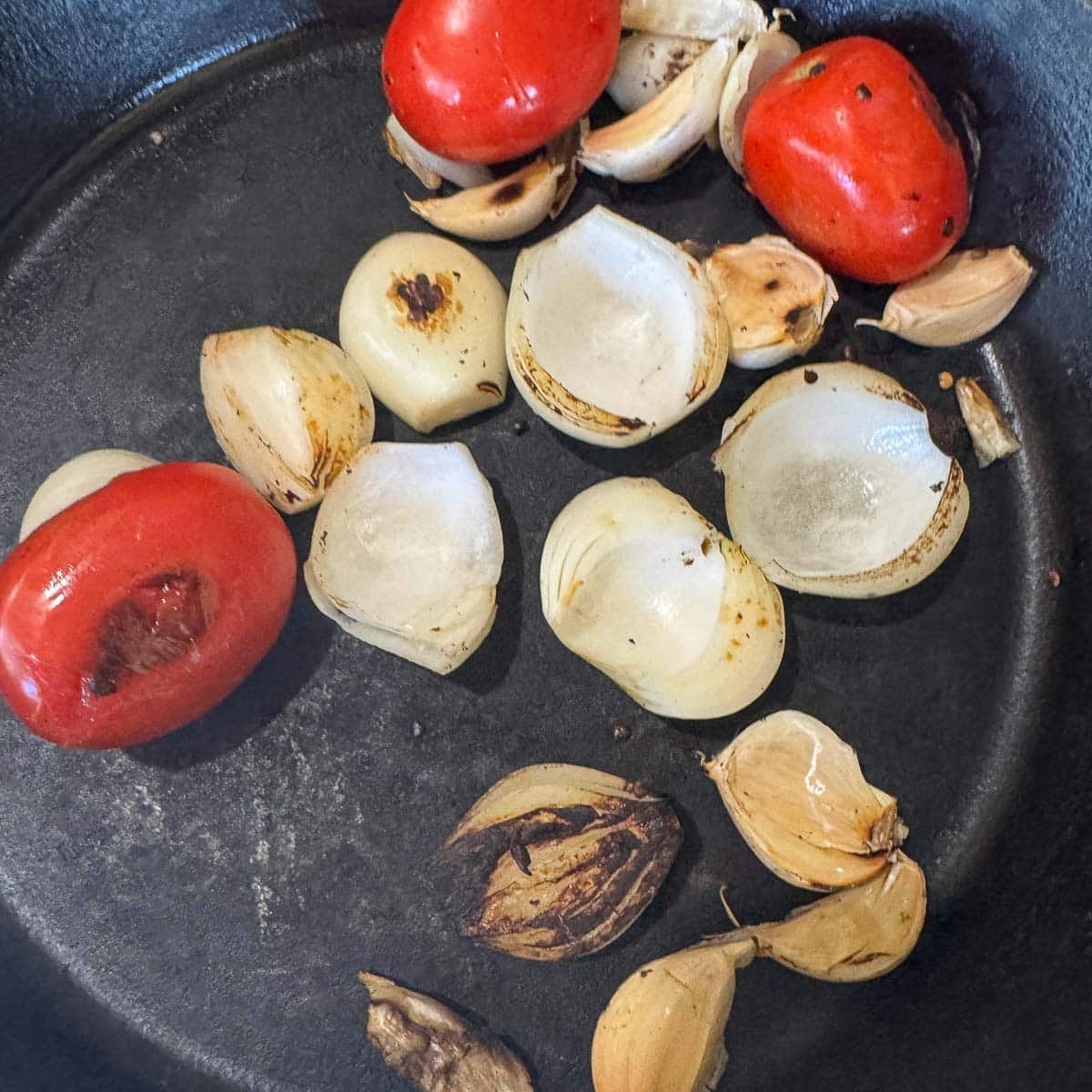 tomatoes, onion, and garlic being charred in a pan