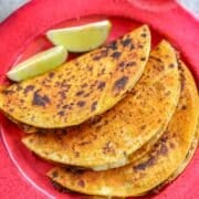 barria tacos with lime wedges on a red plate.