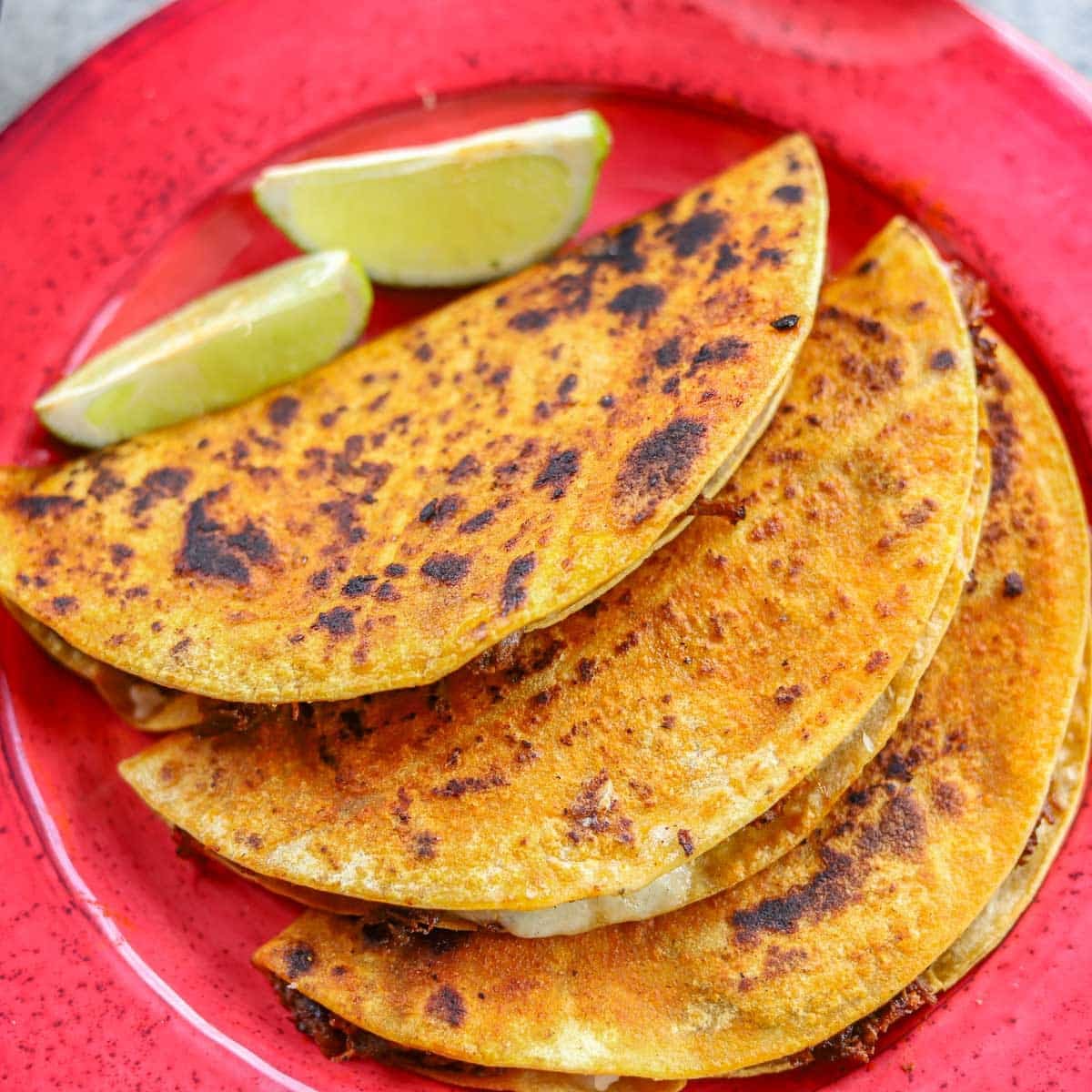 barria tacos with lime wedges on a red plate.