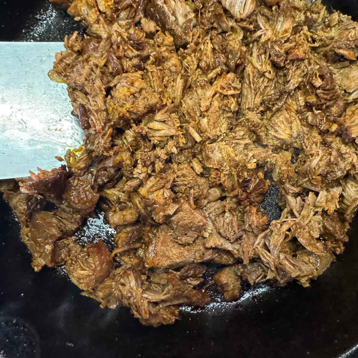 shredded birria being seared in a pan