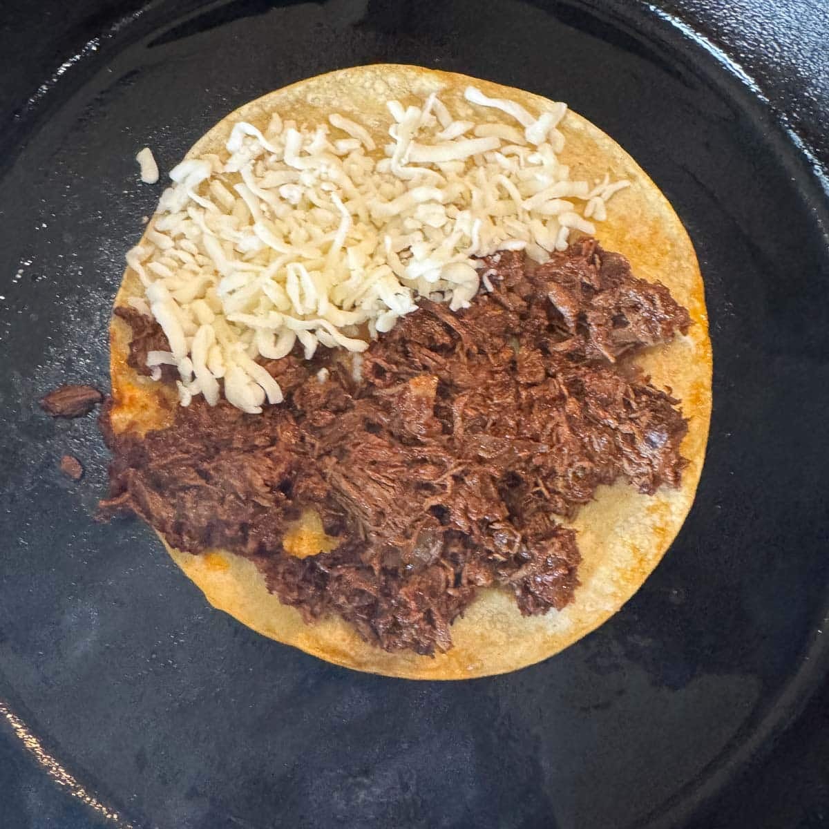 birria and cheese on a tortilla in a pan