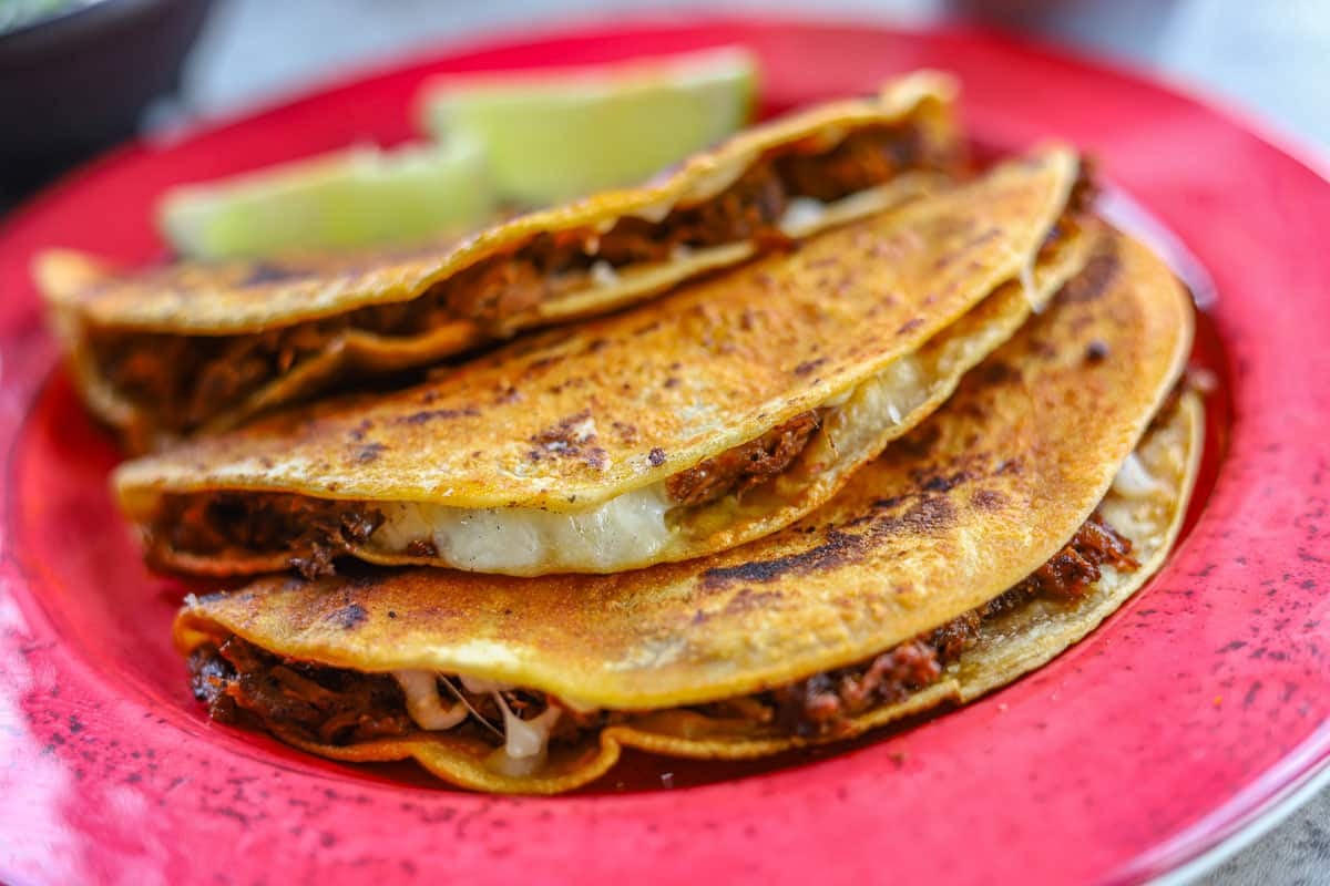 birria tacos on a red plate with lime wedges