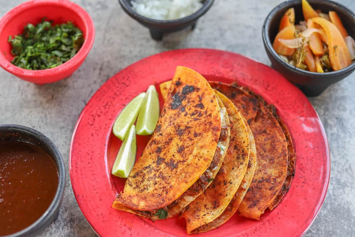 birria tacos on a red plate with sides