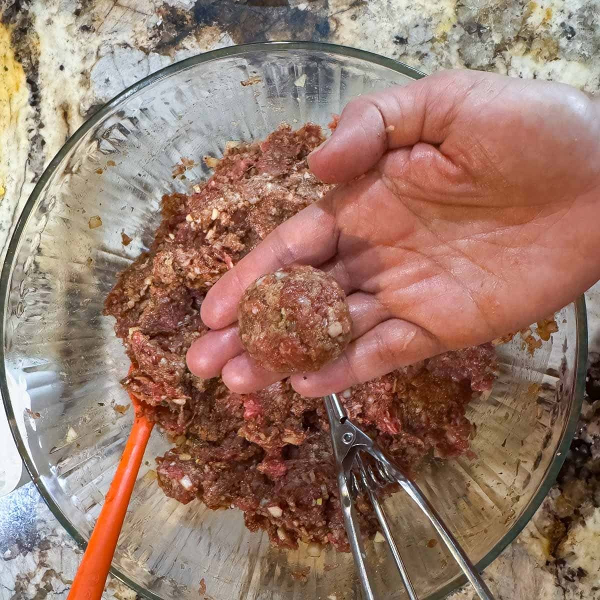 meatball being held over a bowl of meatball mixture