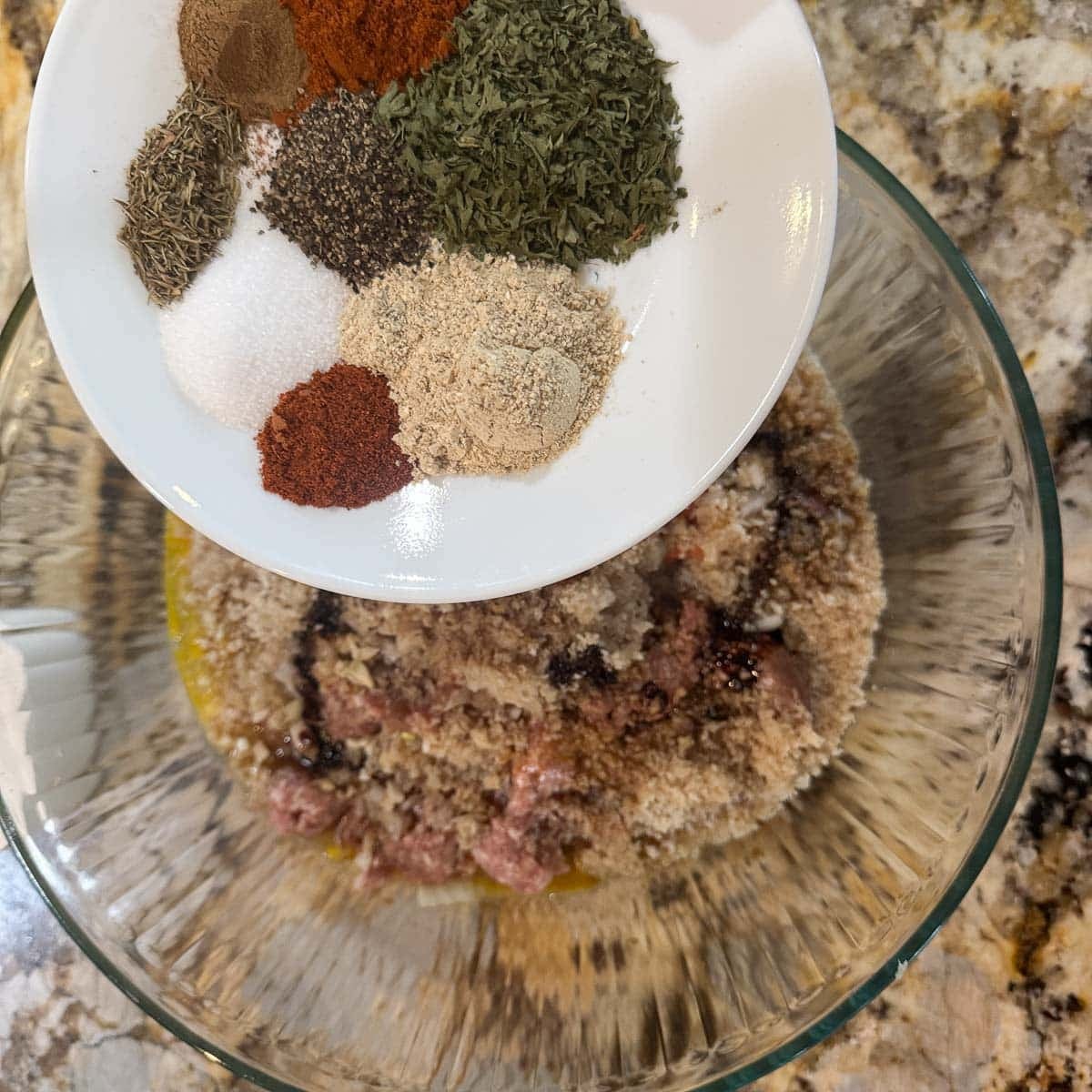 meatball ingredients in a bowl with spices being added to it.